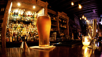 image of filled pint glass with cold blonde beer in foreground and fully stocked elegant bar in background